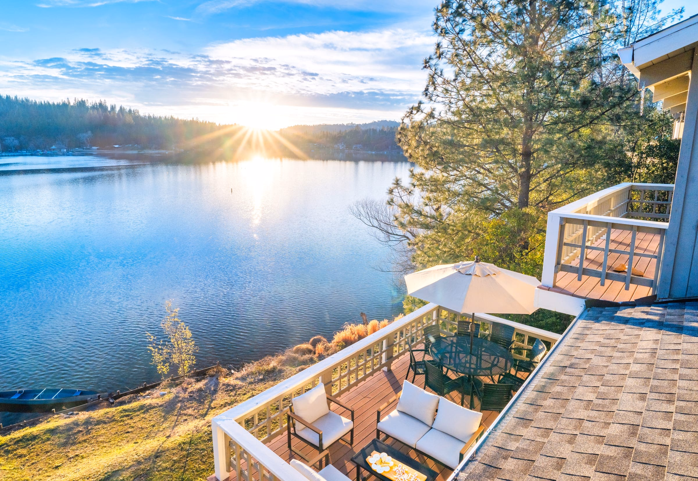 Sun low over Pine Mountain Lake seen from the deck, with an umbrella, table and two chairs in the foreground