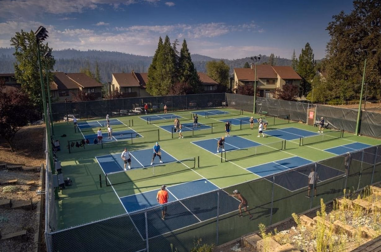 Multiple outdoor pickleball courts in use, surrounded by homes and forested hills