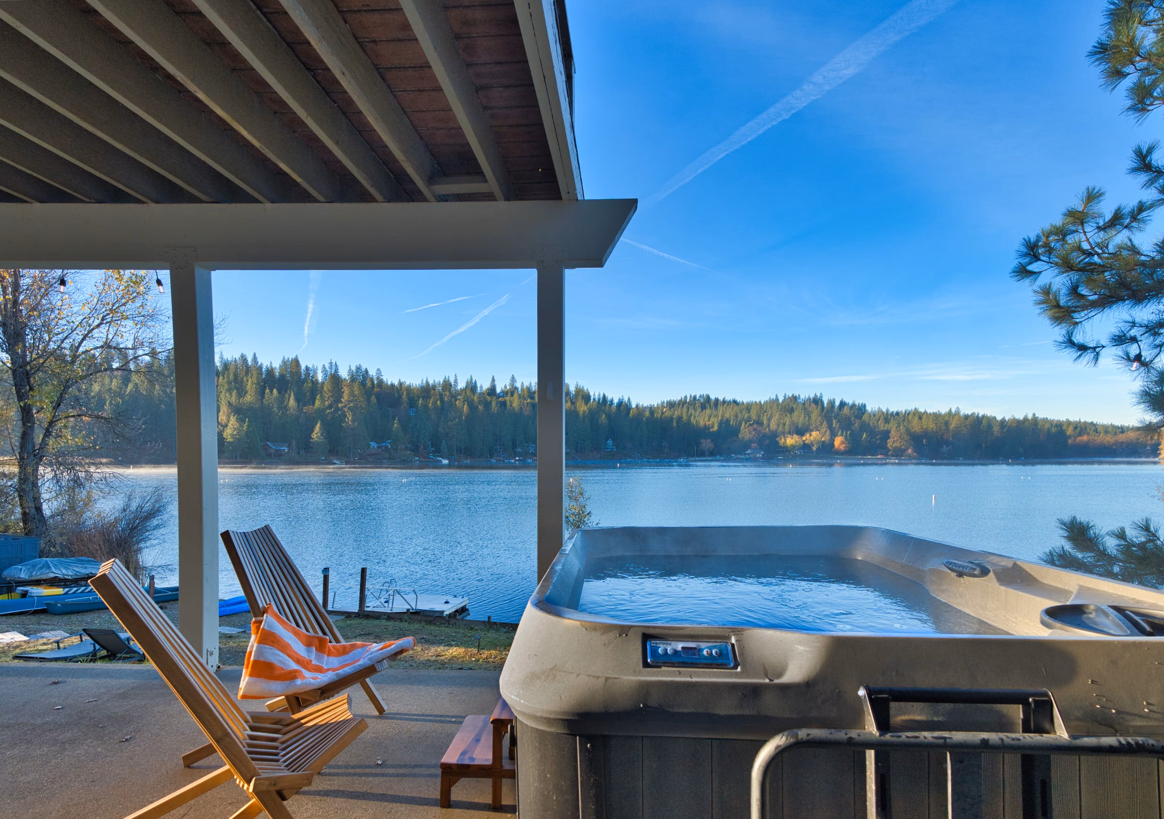 Lakefront hot tub and wooden lounge chairs on a covered patio above the private dock