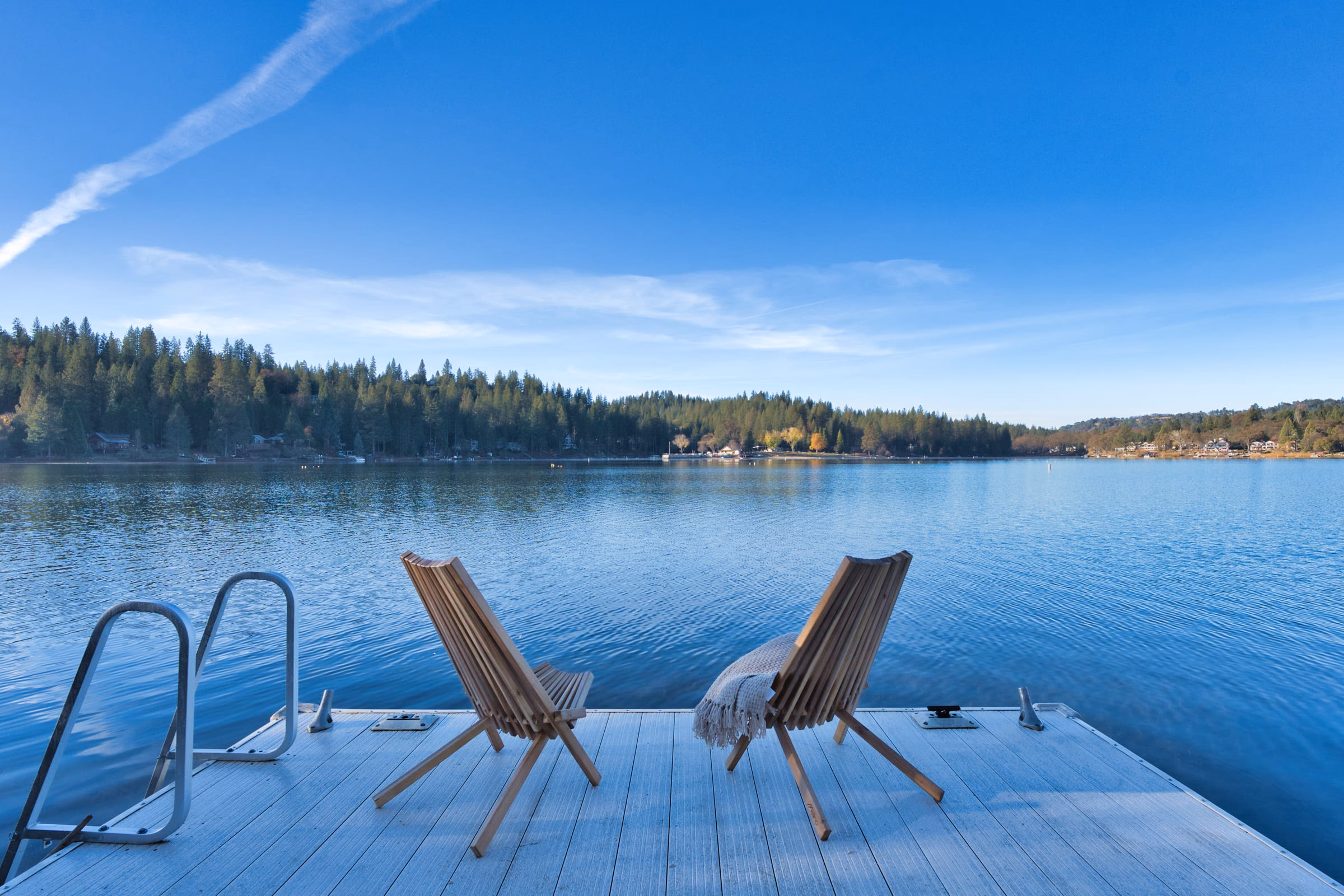 Two wooden lounge chairs and a swim ladder on the private dock over clear blue lake water