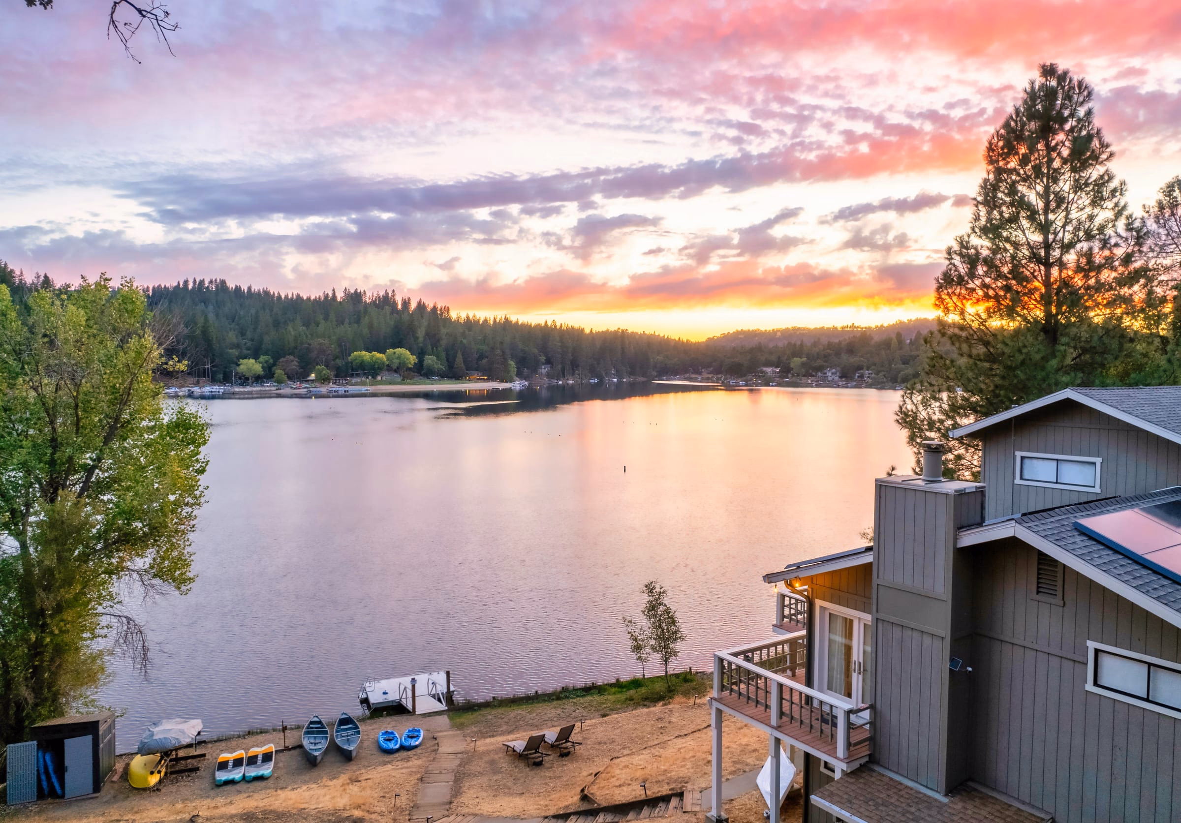 Pink and orange sunset over Pine Mountain Lake, with the house, private dock and watercraft beside the shore