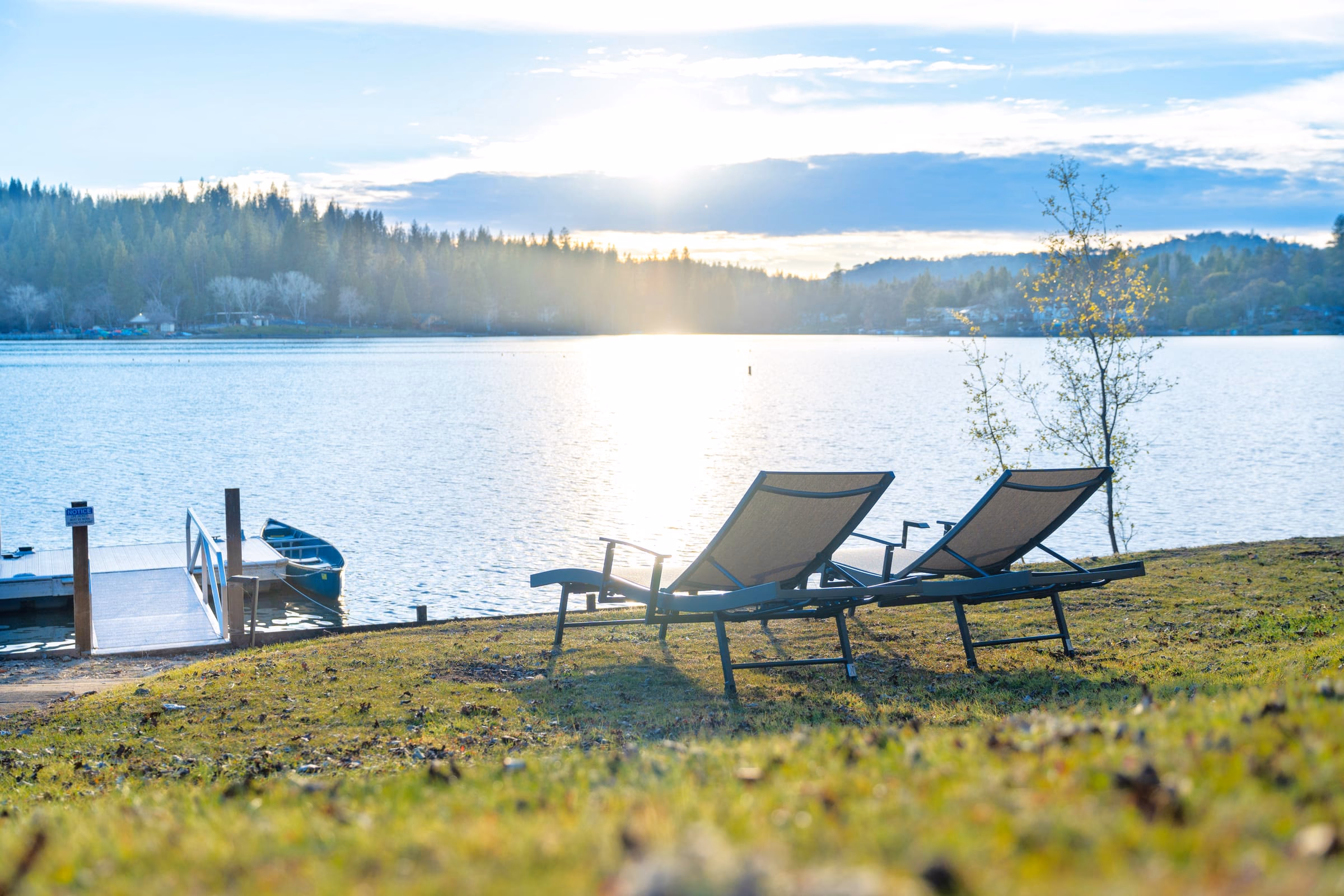 Two reclining chairs on the lakeside lawn facing the private dock and low sun over the water