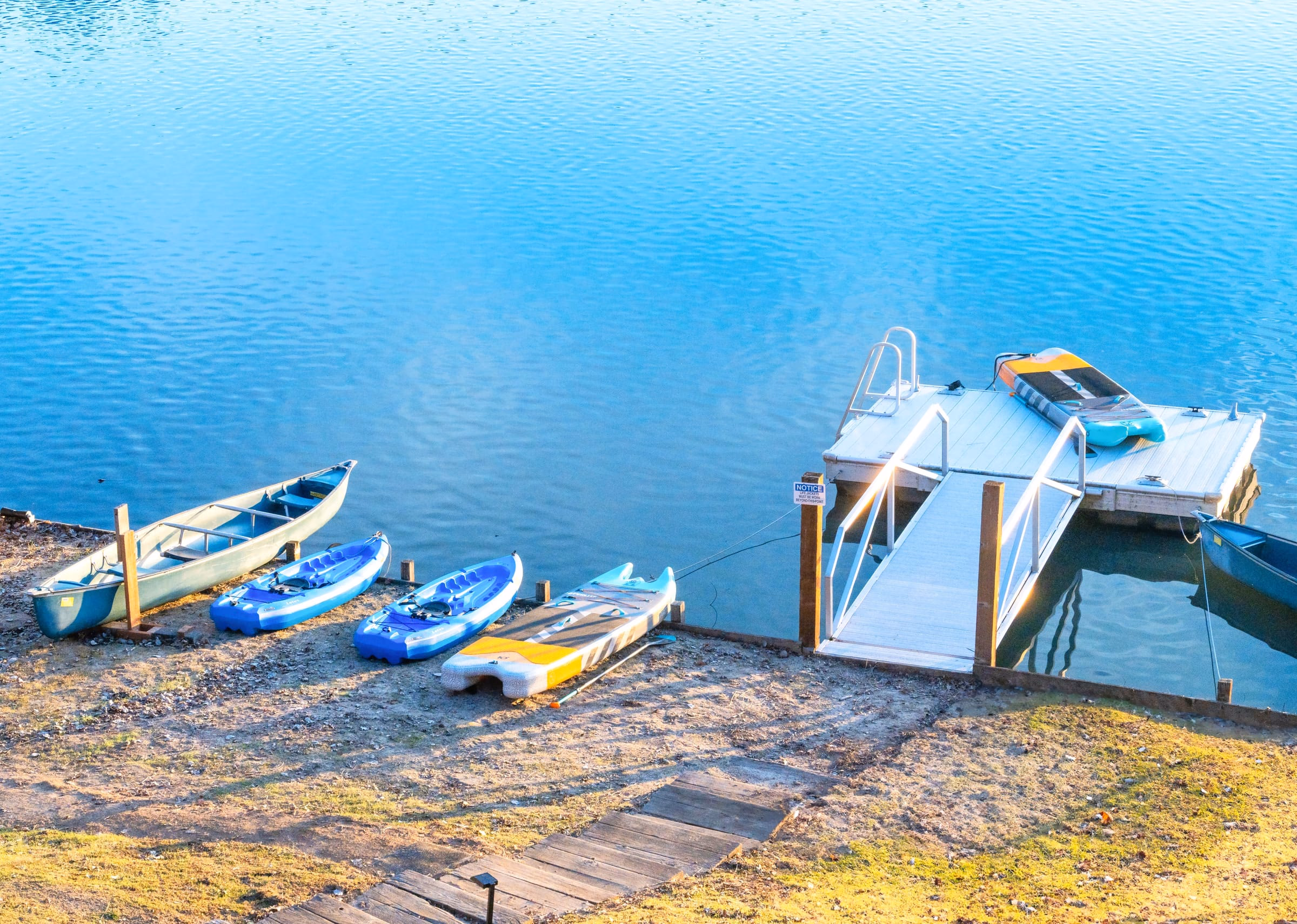 Private dock with a swim ladder, canoes, kayaks and paddleboards arranged along the shore