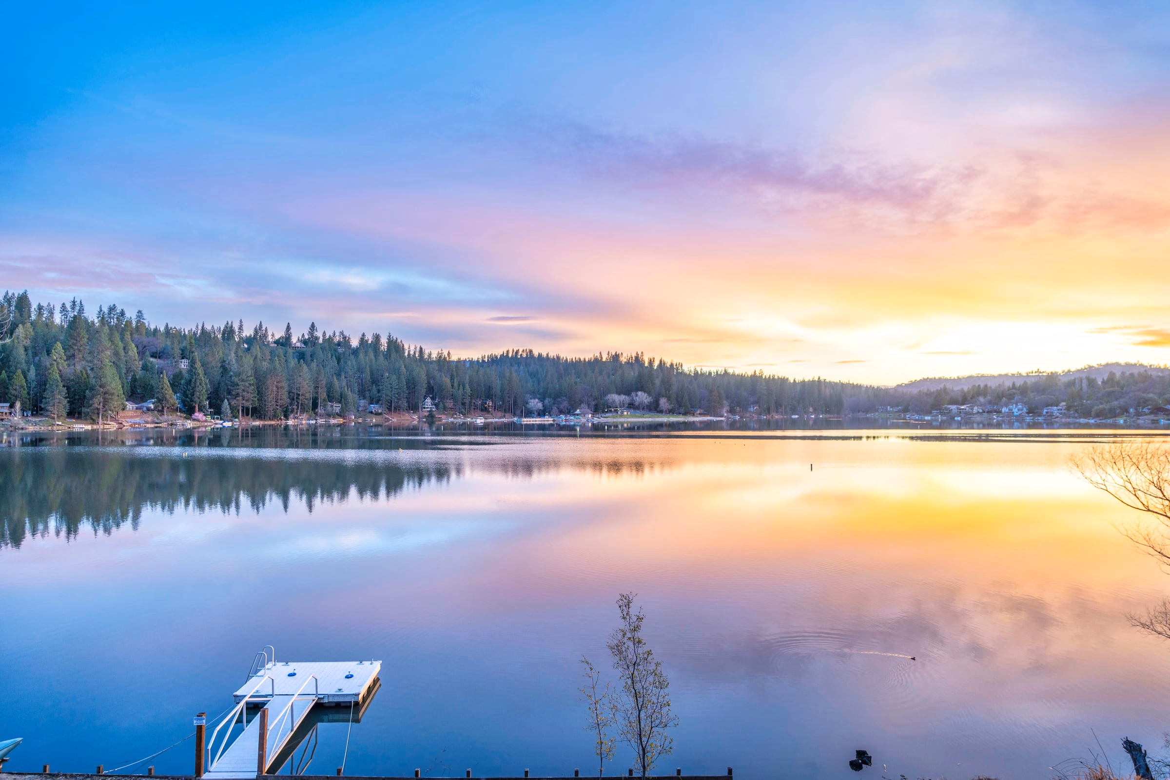 Private dock extending into still water beneath a pink, blue and gold sunset