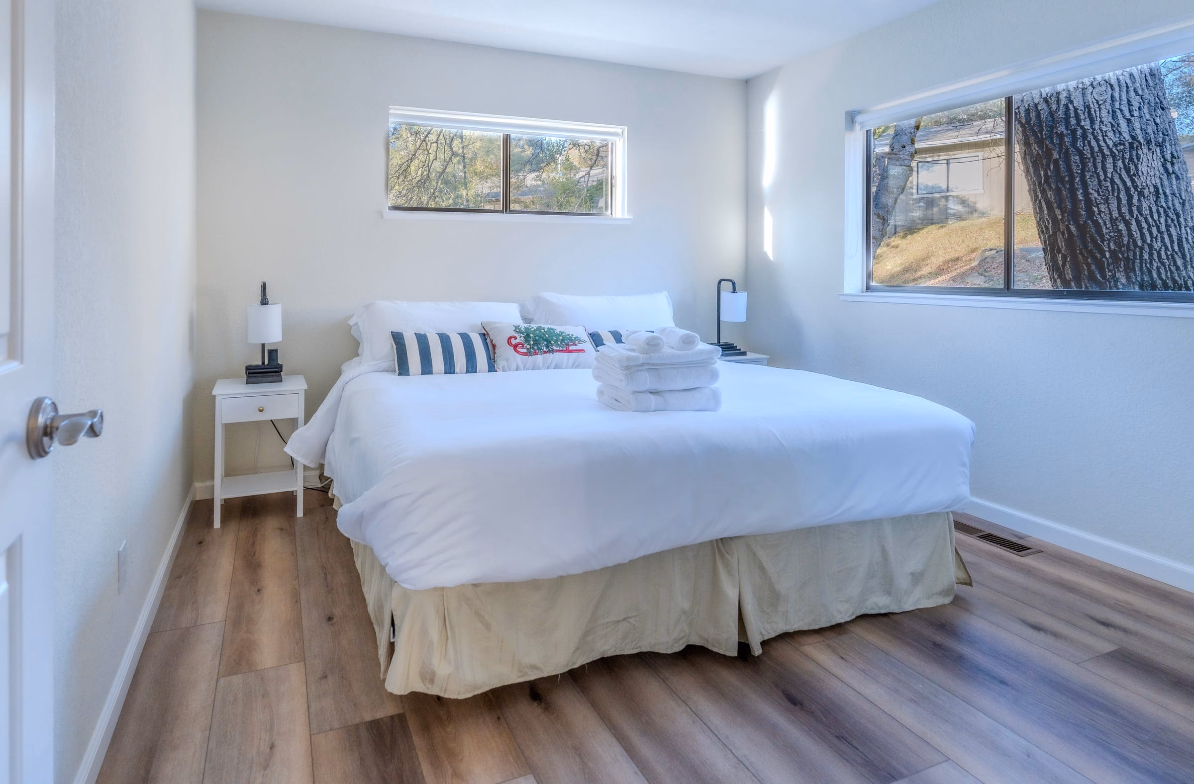 Bright guest bedroom with a large bed, two bedside tables and windows looking onto mature trees
