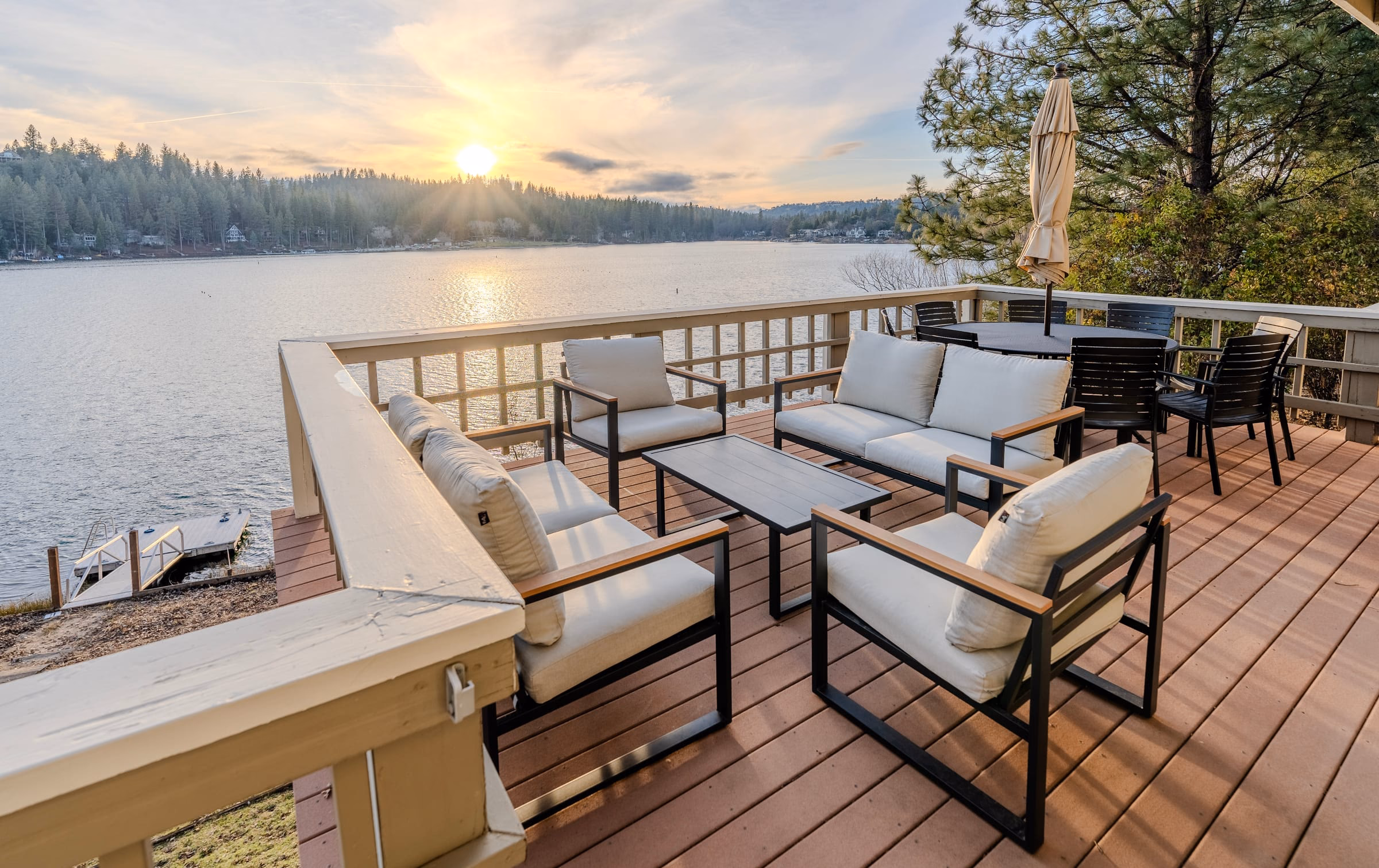 Outdoor sofas and dining chairs on a lakefront deck facing the low sun over Pine Mountain Lake