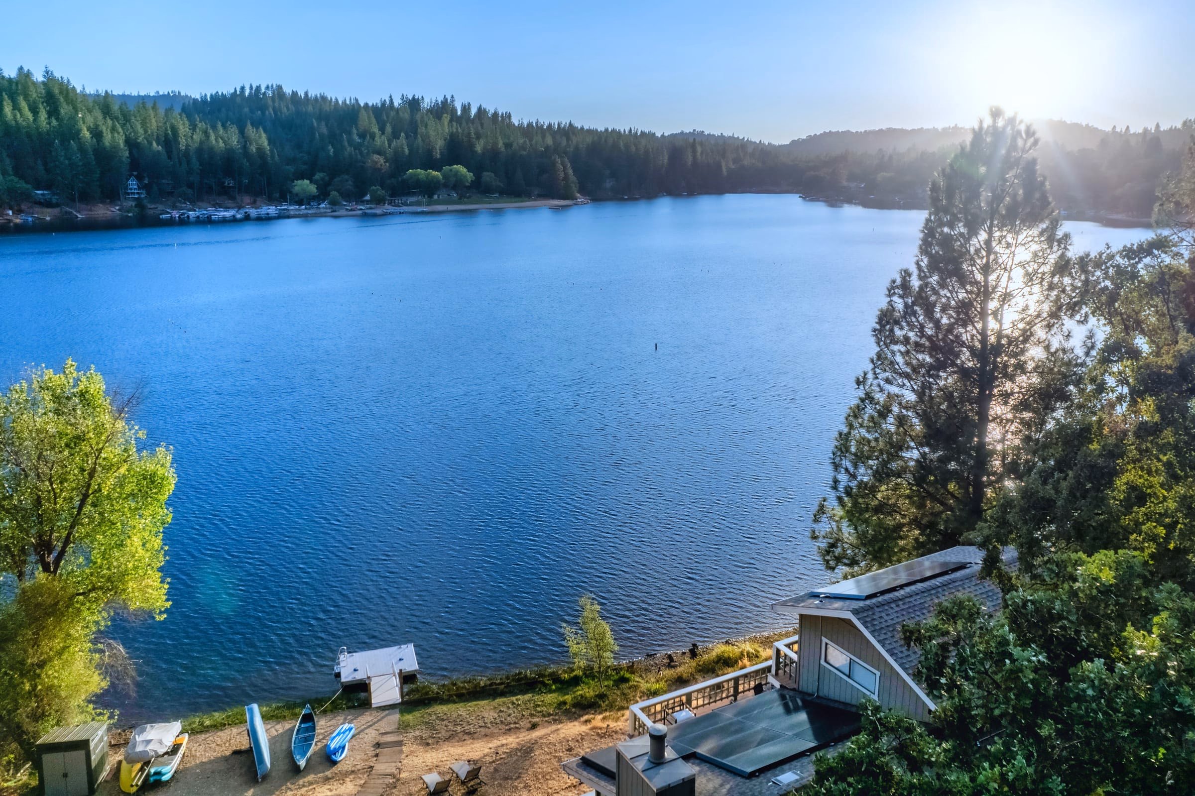 Elevated view across blue water to the forested shoreline, with the private dock and boats below
